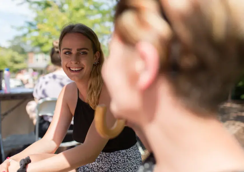 Two students laugh sitting next to each other outside