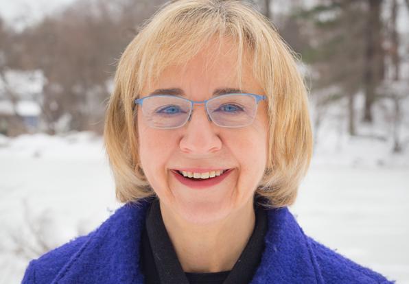 A headshot of Alice Diamond. She has short blonde hair and glasses, is wearing a dark blue coat and there is snow in the background. 